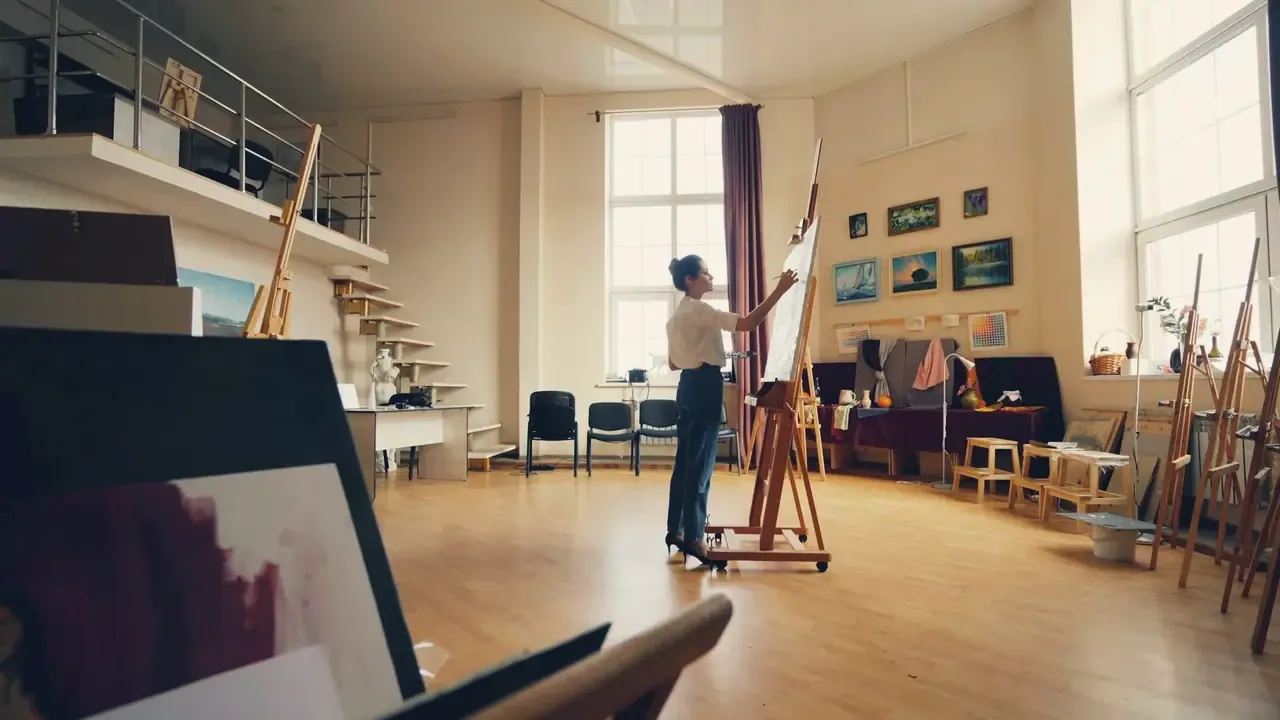 An artist painting at a full-size easel in a double-height loft studio