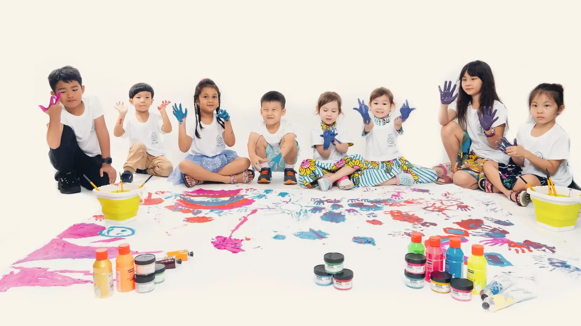 Young artists raising paint-covered hands around one big floor painting