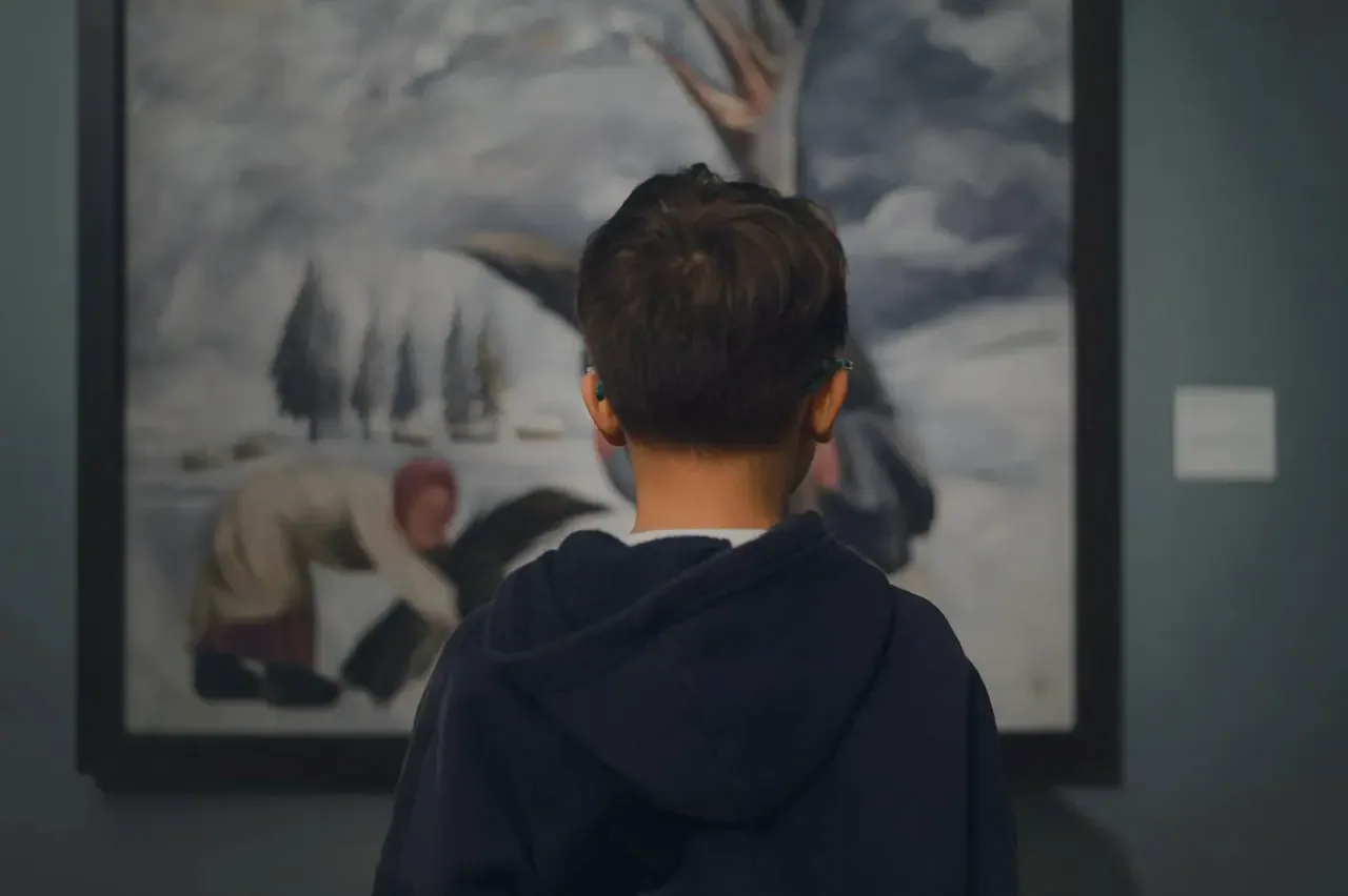 A boy looking up at a large framed landscape in a museum