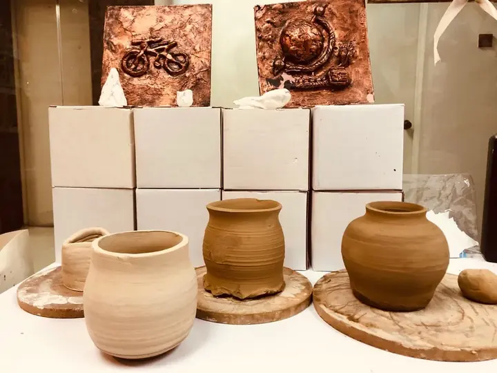 Wheel-thrown clay pots in front of two copper relief plaques
