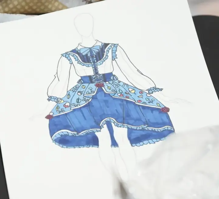 A fashion design illustration of a blue ruffled dress on the studio table beside fabric swatches