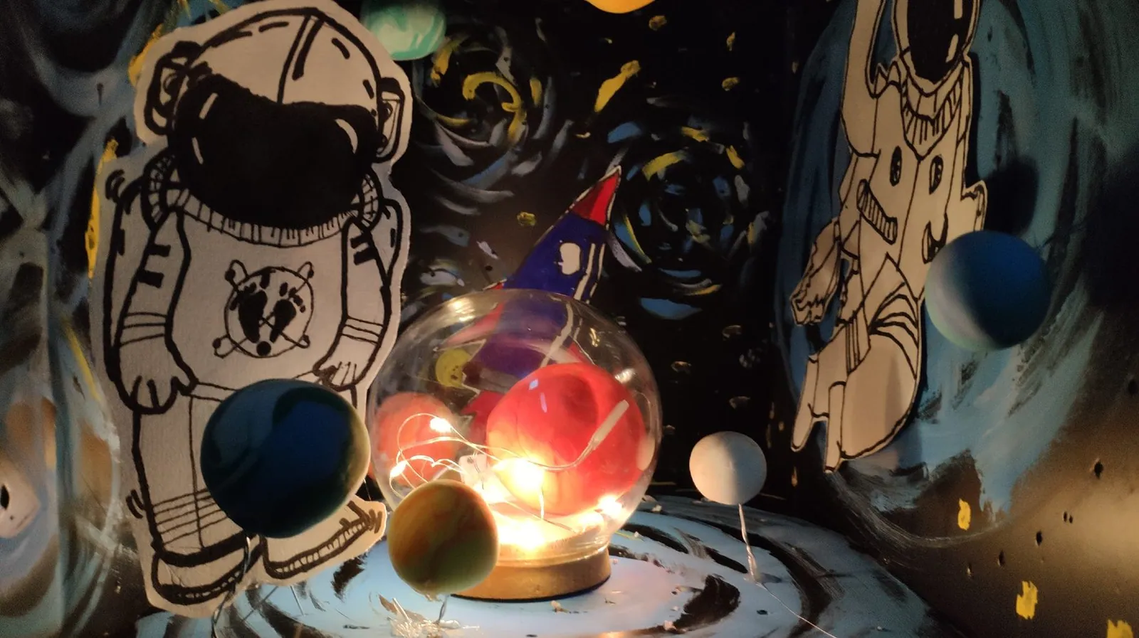 Clay planets and cut-paper astronauts around a glowing glass-sphere lamp