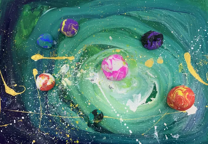 A swirling acrylic galaxy with marbled clay planets