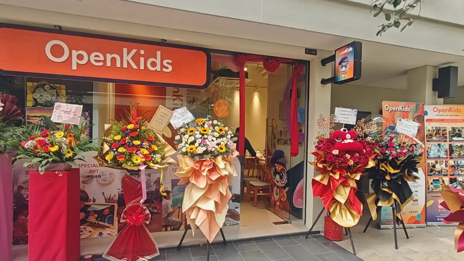 The OpenKids Art DesaPark Campus in Kuala Lumpur on opening day, its orange OpenKids sign above a shopfront lined with opening flower stands