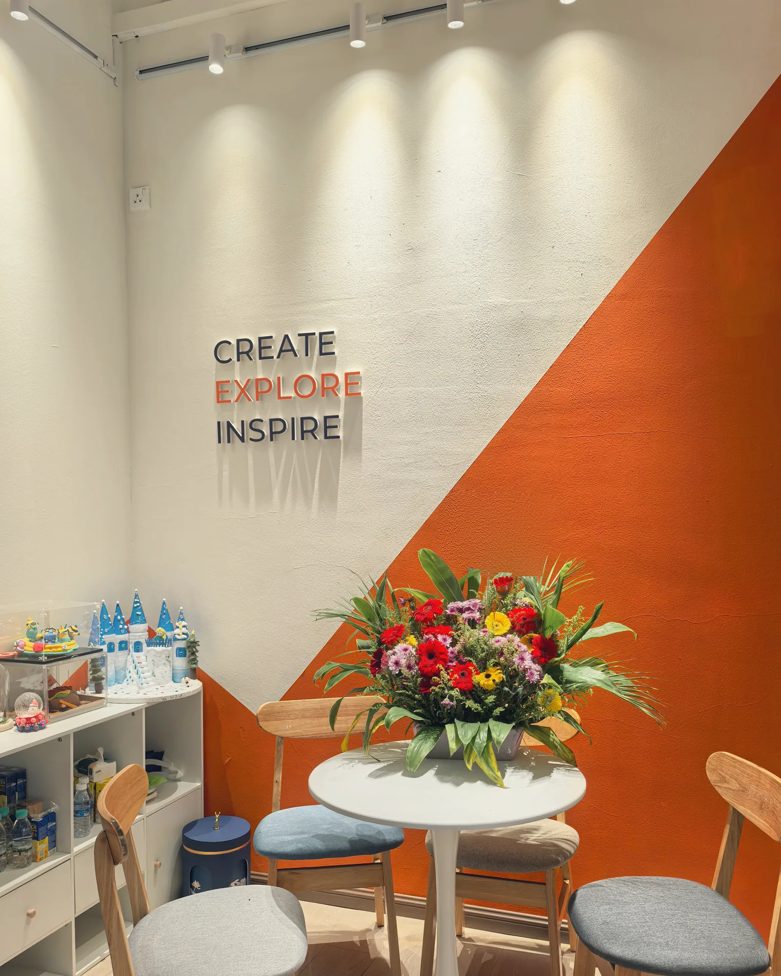 The reception of an OpenKids campus in Kuala Lumpur: the words Create Explore Inspire on an orange wall, flowers on the table