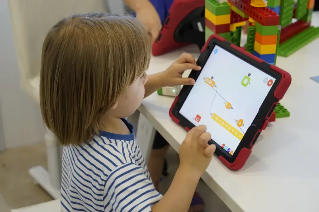 A young child programs on a tablet beside a big-brick build