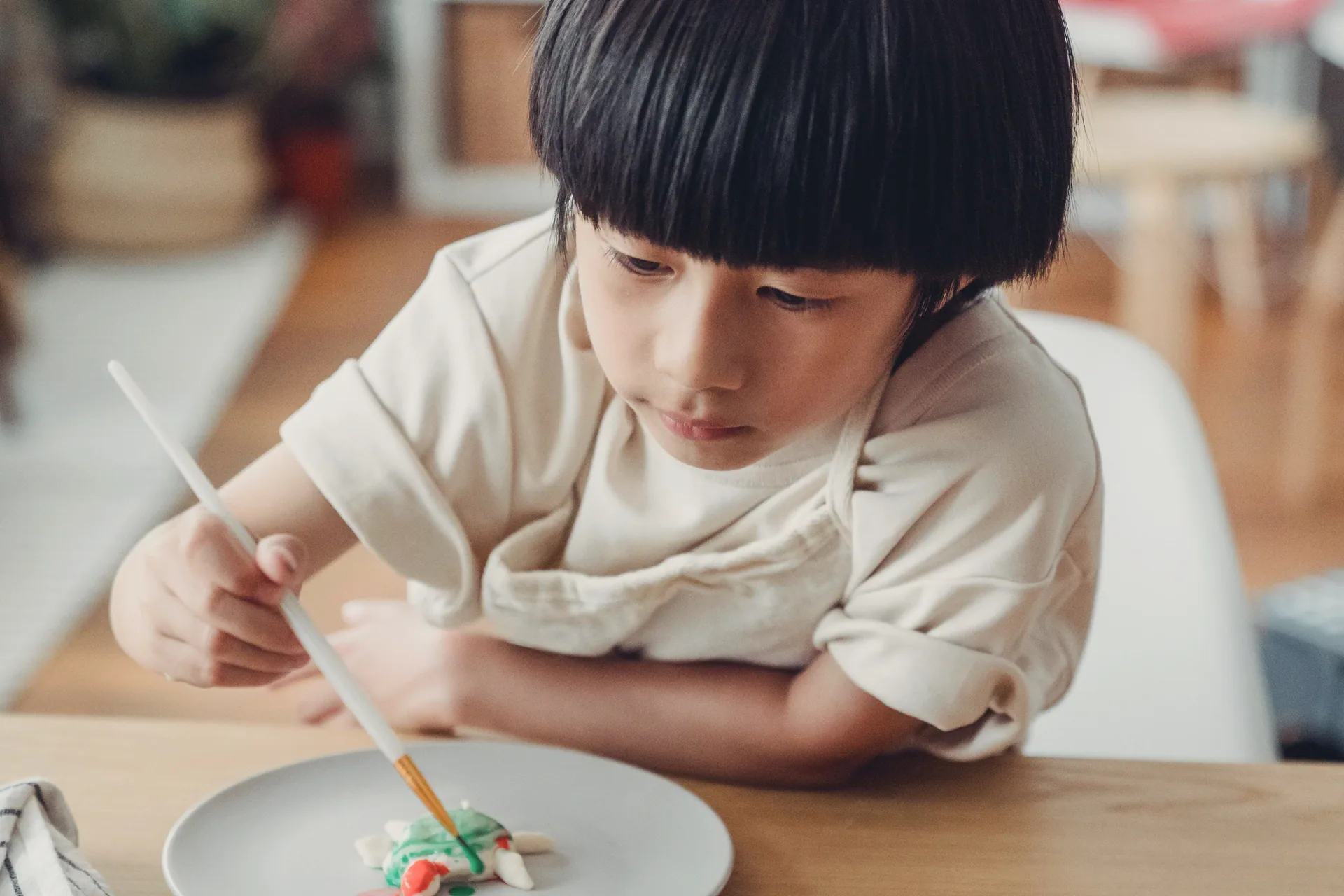 A boy painting a small clay figure on a plate, absorbed in the brushwork