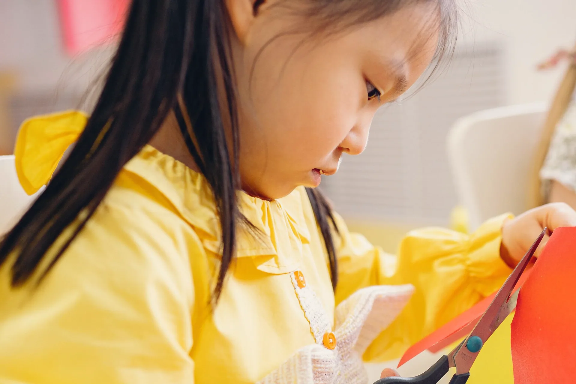 A girl in a yellow smock cutting red paper with scissors