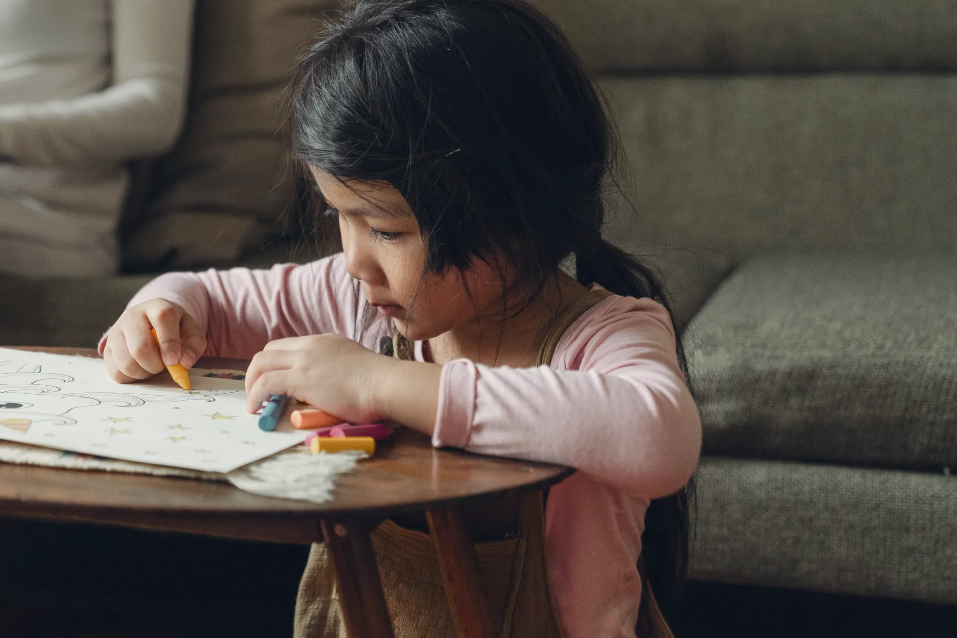 A young girl colouring at a low table while her mother works on a laptop nearby