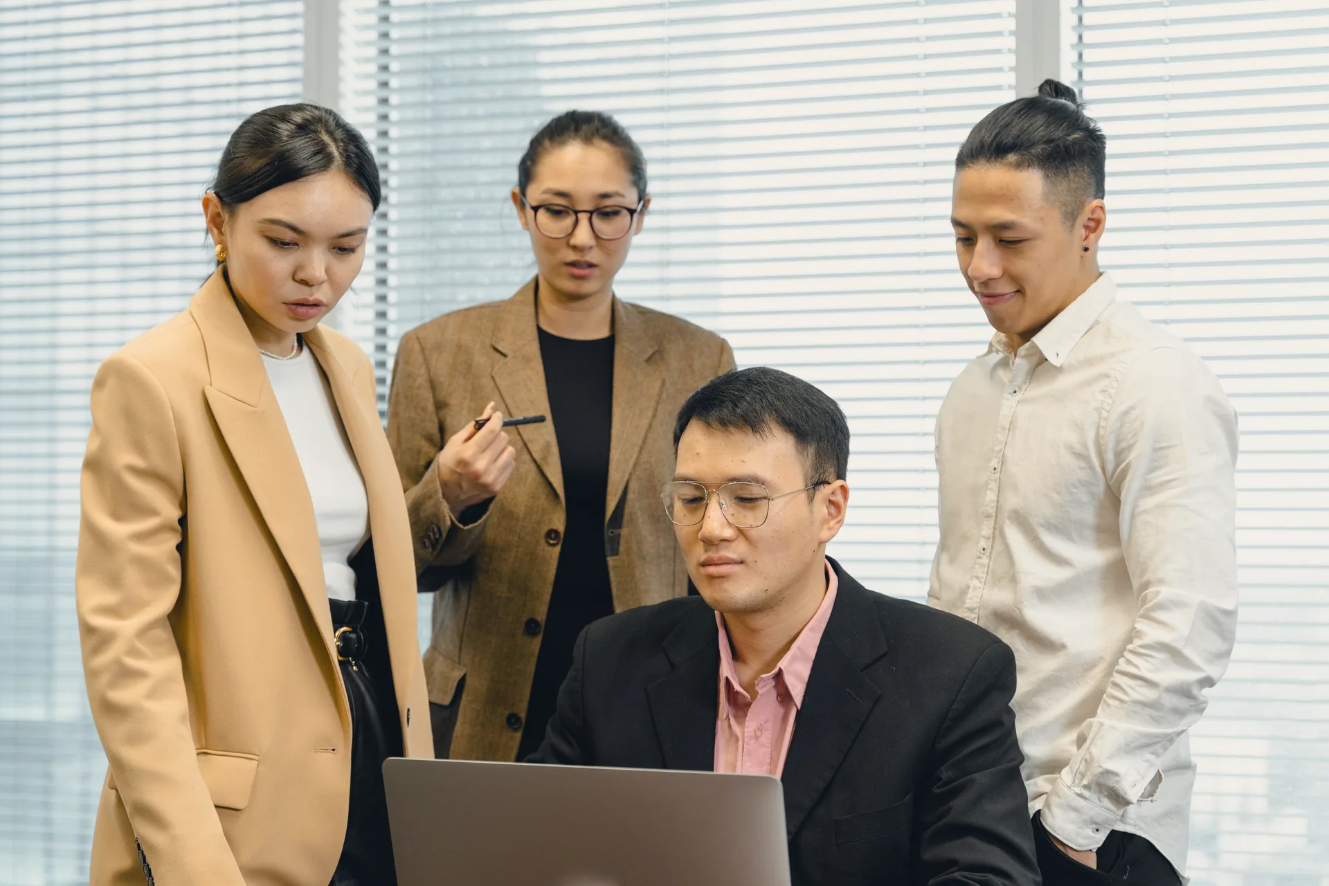Four colleagues gathered around a laptop in a bright office