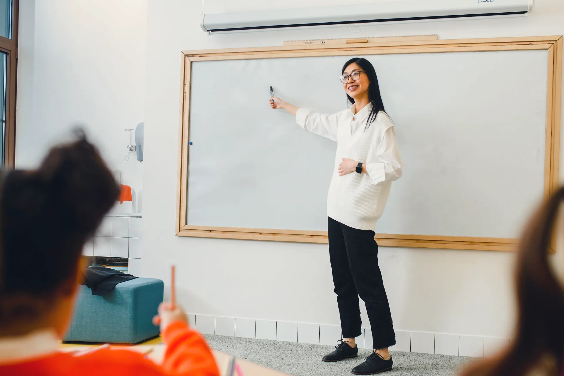 A teacher at the whiteboard leading a class in a bright classroom