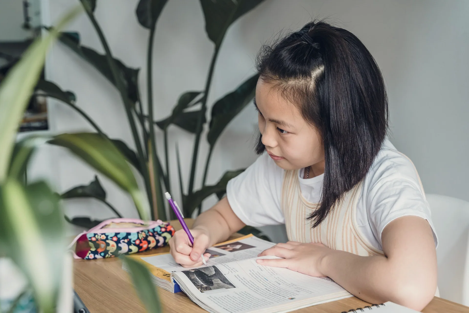 A girl writing in her workbook at a sunny wooden table