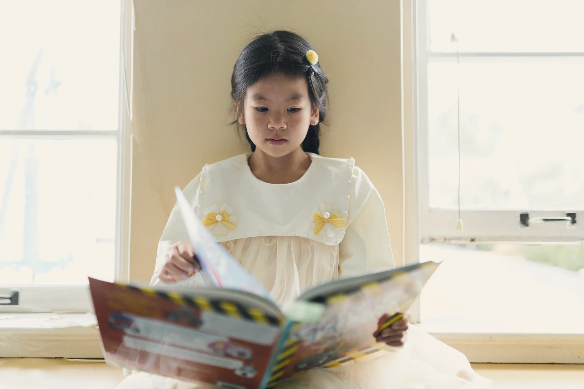 A girl reading a picture book by a bright window